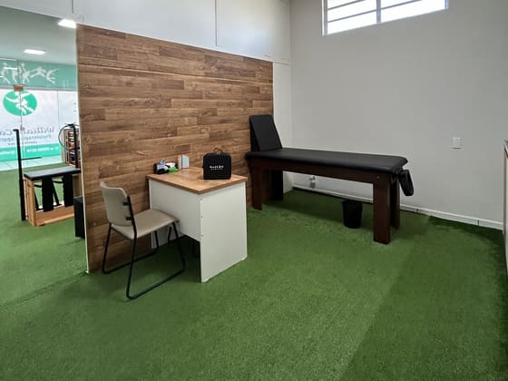Sala de avaliação da clínica, com maca, mesa e parede de madeira.
